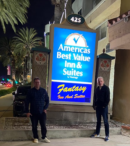 Ian Lloyd and Doc Swallow posing beside the Fantasy Inn and Suites sign