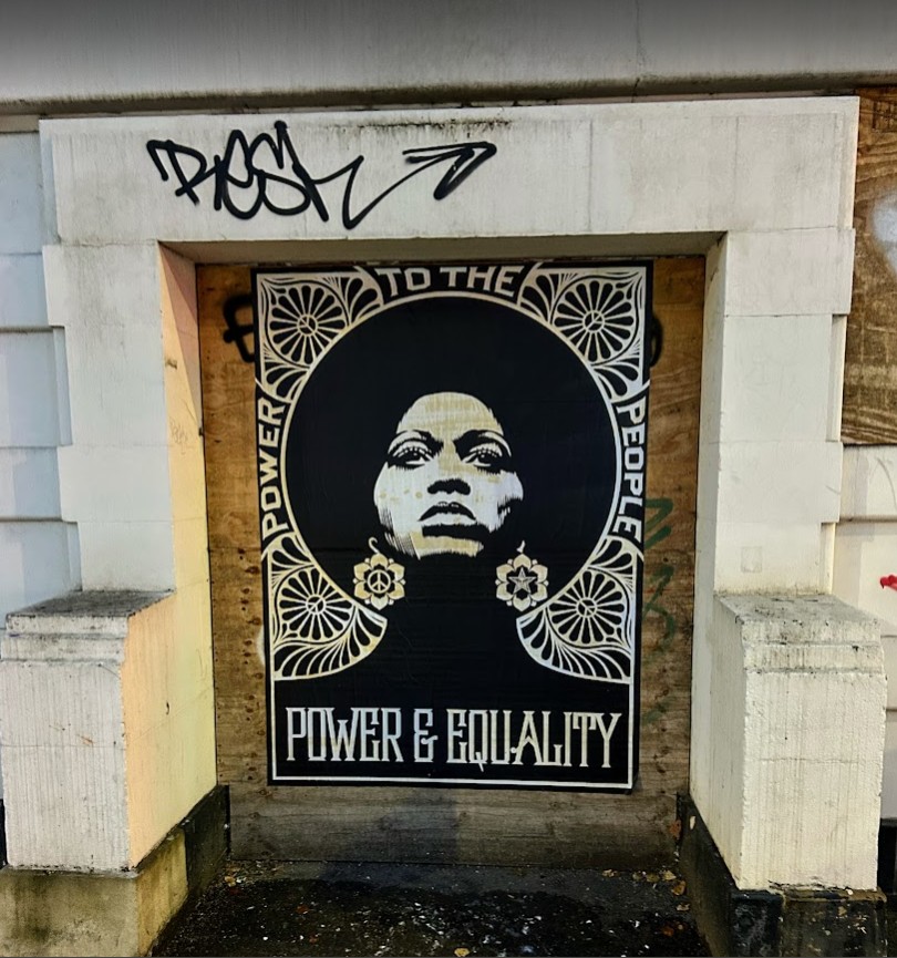 a large, black-and-white poster of a black woman with a powerful, contemplative expression. Surrounding her are intricate floral designs, adding to the bold visual impact. The words 