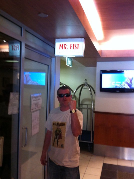 Bruce in a shopping mall in Perth Western Australia, poses with his fist below a sign for a shop "Mr Fist"