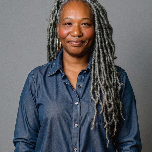 Protrait pic of Natalie, they have long flowing dreds and a blue semi-formal shirt