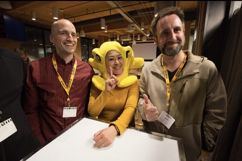 Scott smiling far right. In the middle is Junko wearing a yellow costume (looks alien). Next to her is Adrian smiling. A good vibes pic from a11yTO.