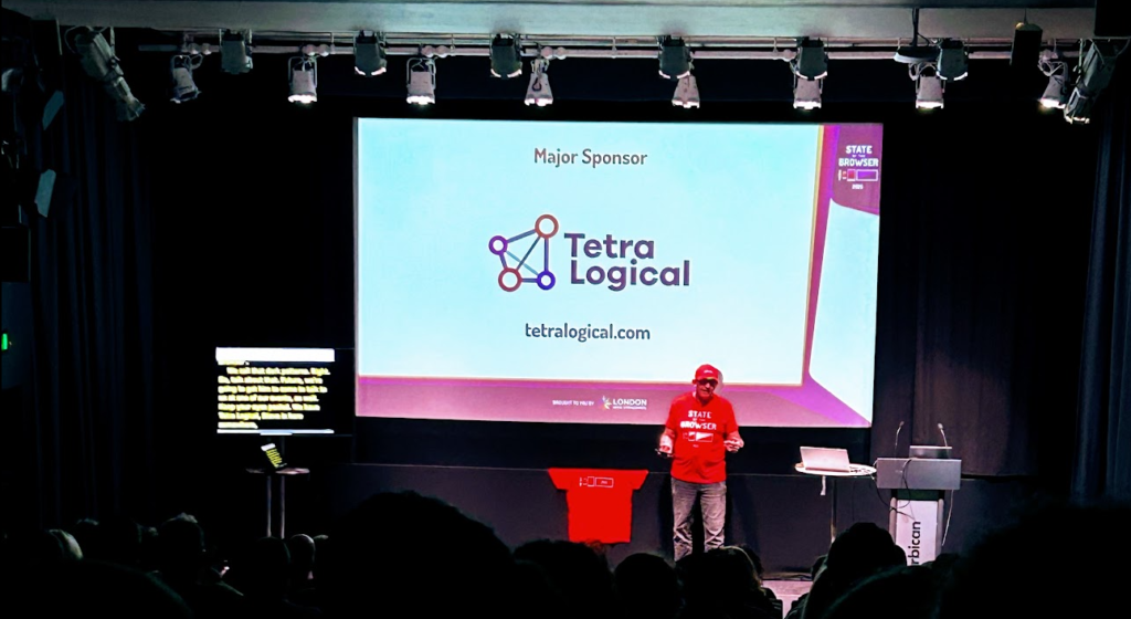 Dave on stage at SOTB 2025, in front of a giant screen declaring TetraLogical as a major sponsor.